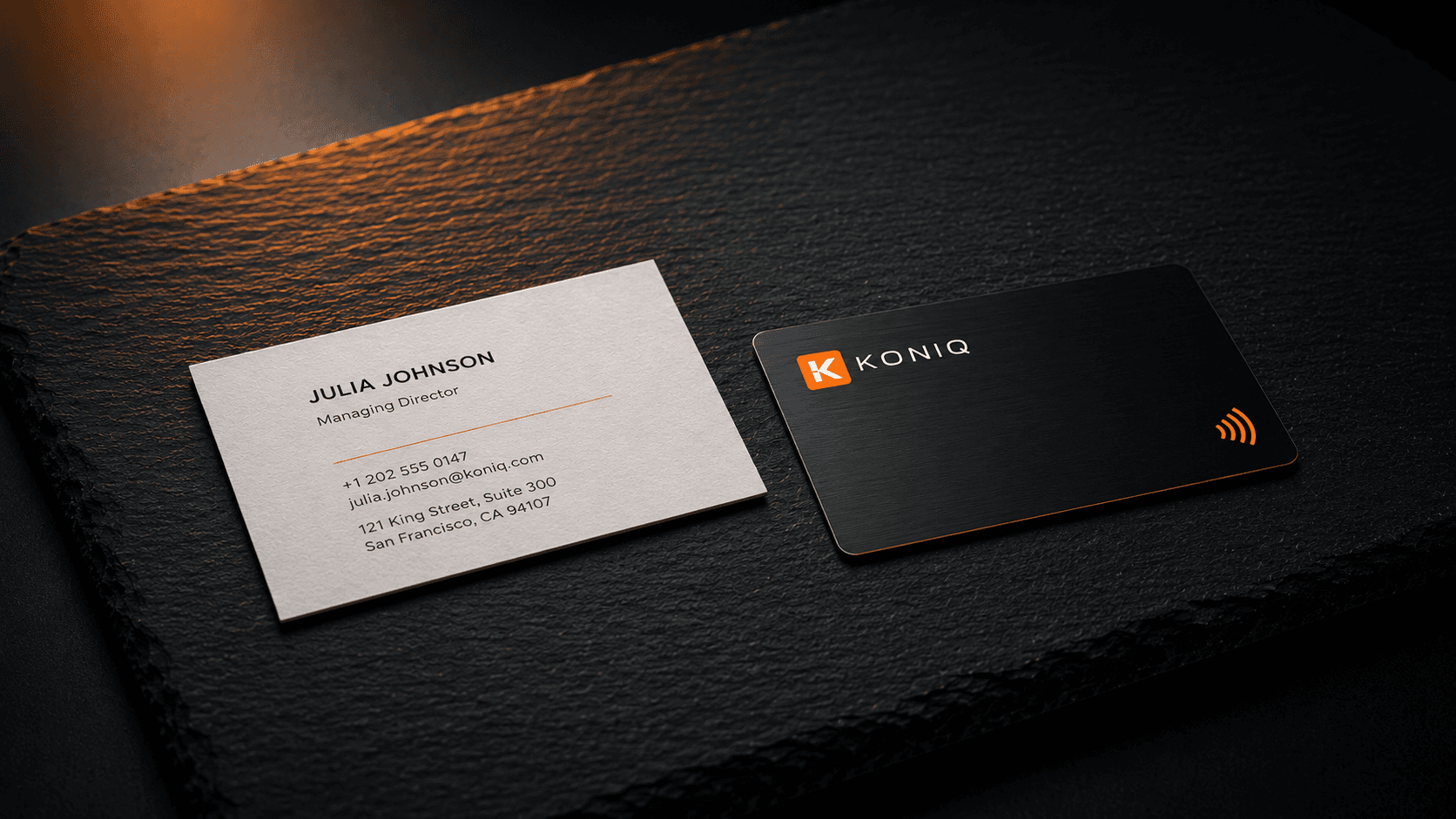 Carte de visite papier classique posée à côté d'une carte de visite KONIQ noire NFC sur une dalle d'ardoise